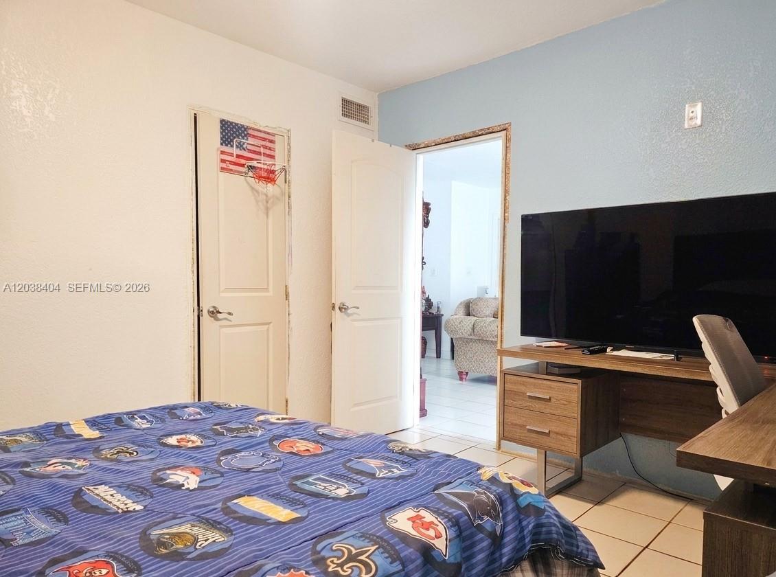 A bedroom features a patterned bedspread, a television on a desk, and an open doorway — HIALEAH, FL