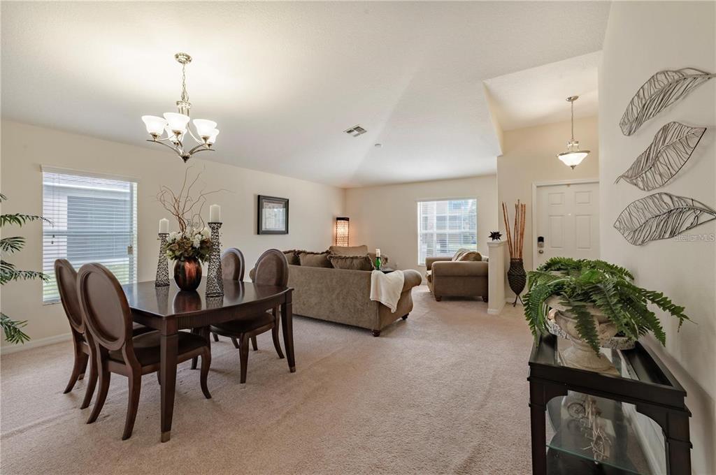 A dining area and living room with beige carpet, neutral walls, and vaulted ceilings — 12116 ECHO BASIN COVE, RIVERVIEW, FL