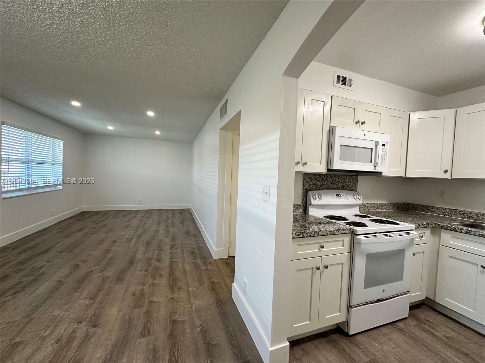 A kitchen with white cabinets and granite countertops opens into a living area with wood-look flooring — 2500 Johnson St # 19, Hollywood FL 33020, HOLLYWOOD, FL