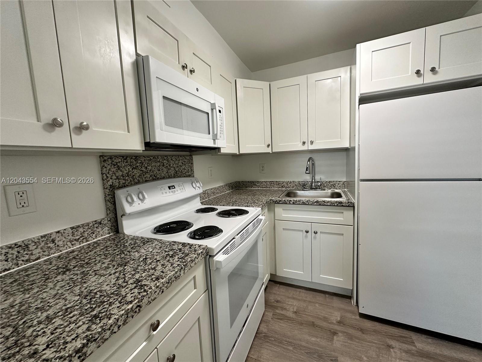 A kitchen features white cabinets, granite countertops, and white appliances on a wood-look floor — 2500 Johnson St # 19, Hollywood FL 33020, HOLLYWOOD, FL