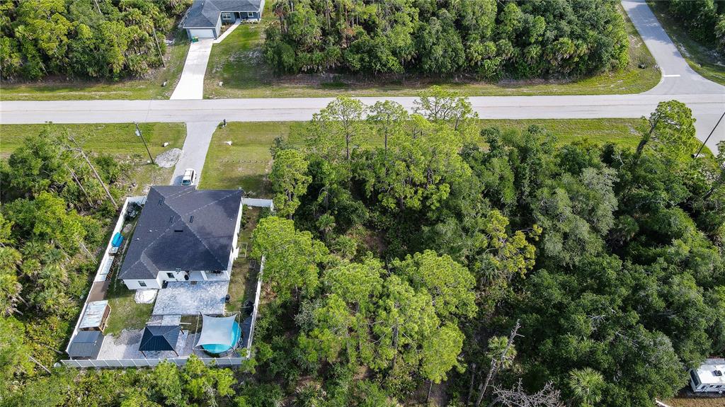 An aerial view shows a house with a fenced backyard next to a wooded lot — 1213 BISCAYNE DRIVE, PORT CHARLOTTE, FL