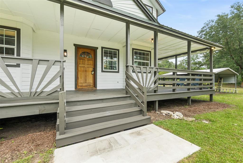 A white house features a grey wooden porch with stairs and a natural wood front door — 2680 W COUNTY ROAD 2006 W, BUNNELL, FL
