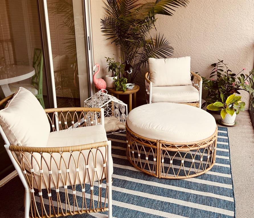 A balcony features two wicker chairs, a round ottoman, and potted plants on a striped rug — 8941 VERANDA WAY UNIT 522, SARASOTA, FL