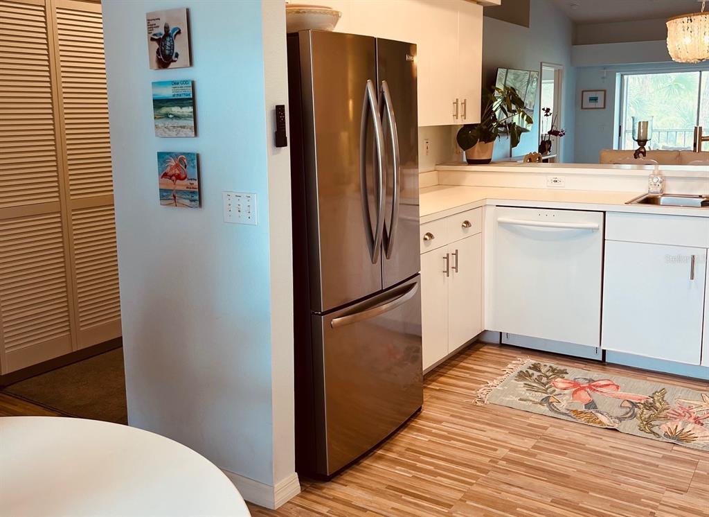 A kitchen features a stainless steel refrigerator, white cabinets, a dishwasher, and wood-look flooring — 8941 VERANDA WAY UNIT 522, SARASOTA, FL
