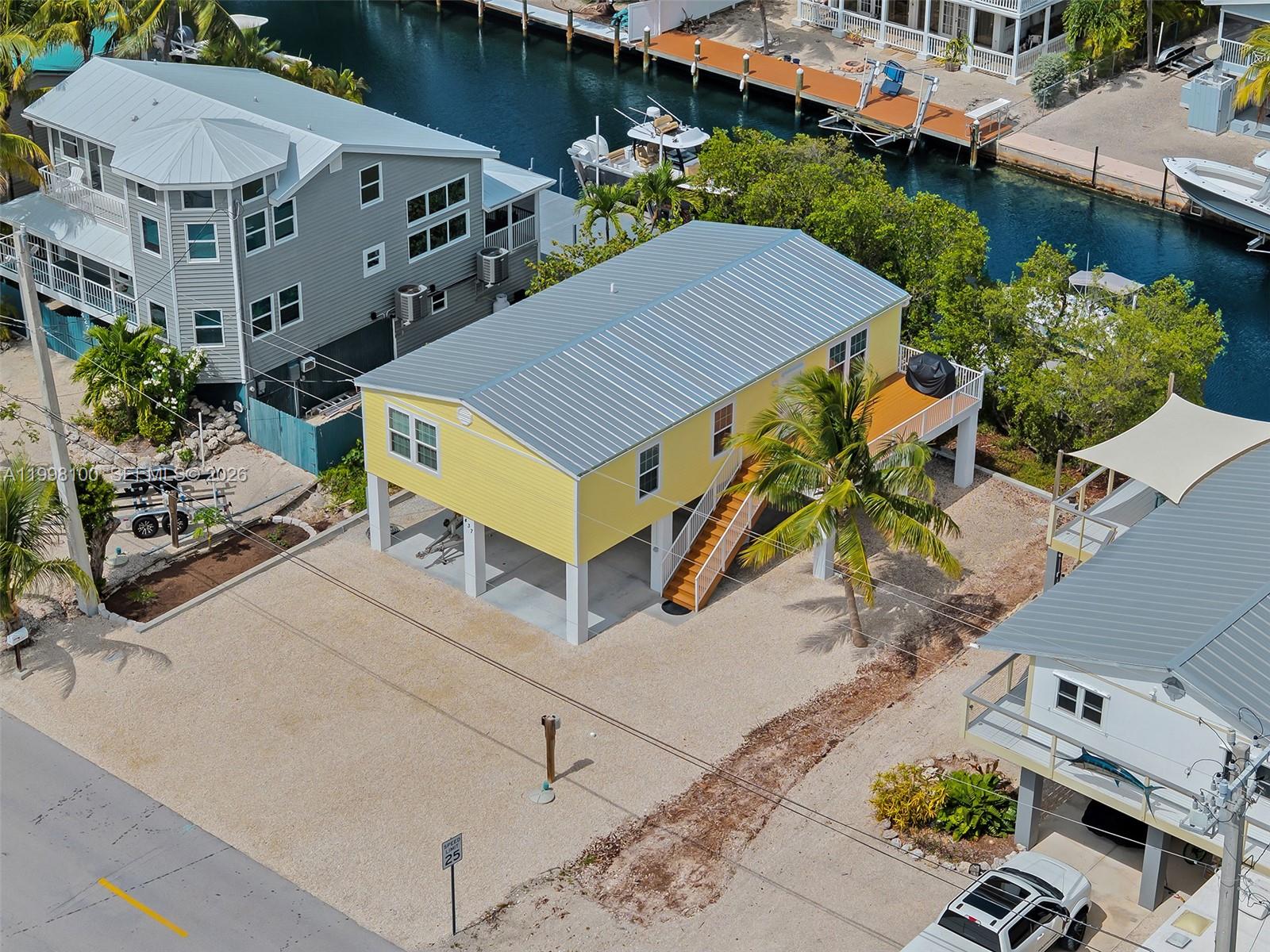 An elevated yellow house with a metal roof sits on a gravel lot near water — 437 Pirates Rd, Torch Key FL 33042, TORCH KEY, FL