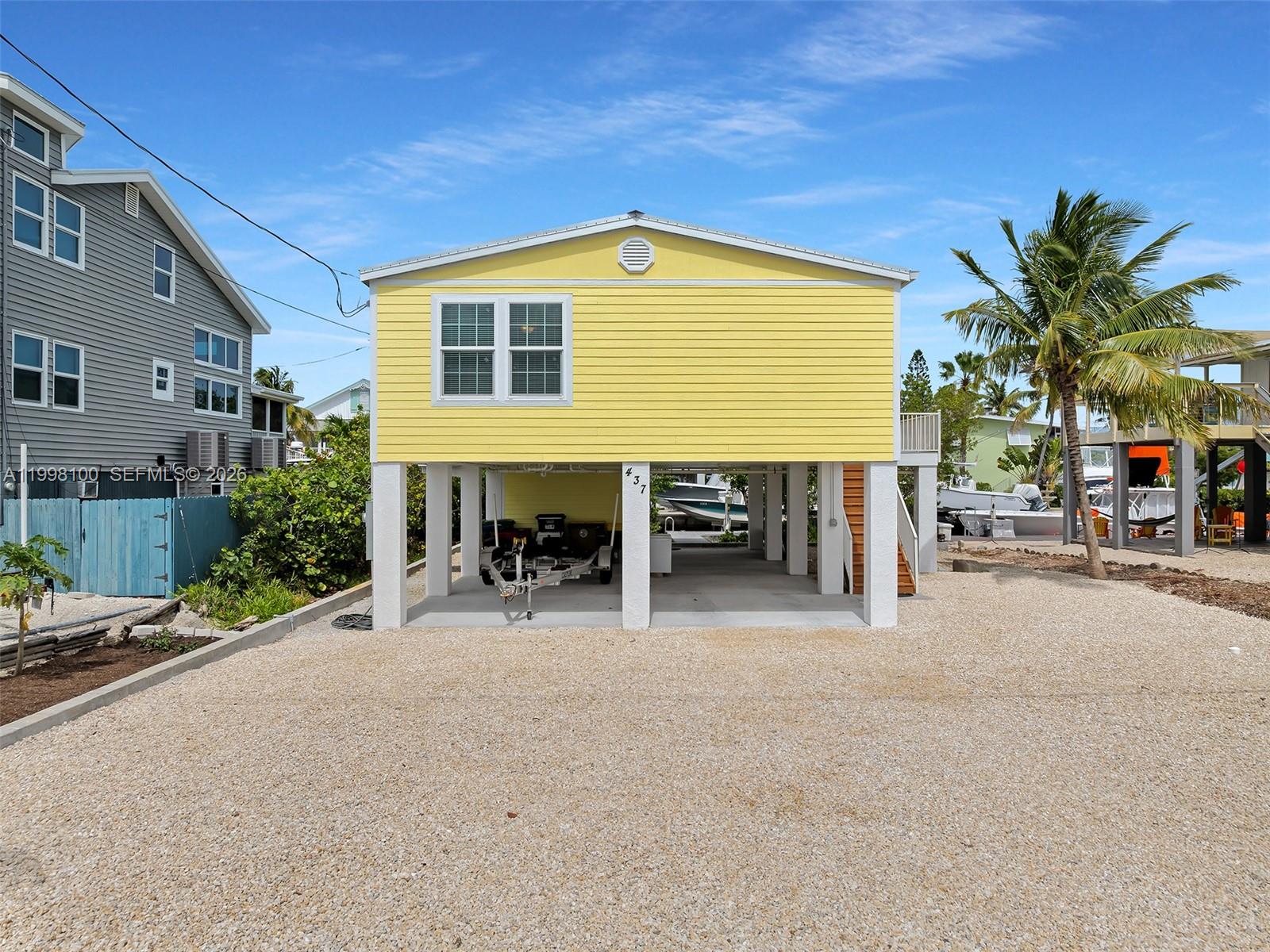 A yellow house on stilts sits above a gravel driveway with a boat trailer underneath — 437 Pirates Rd, Torch Key FL 33042, TORCH KEY, FL