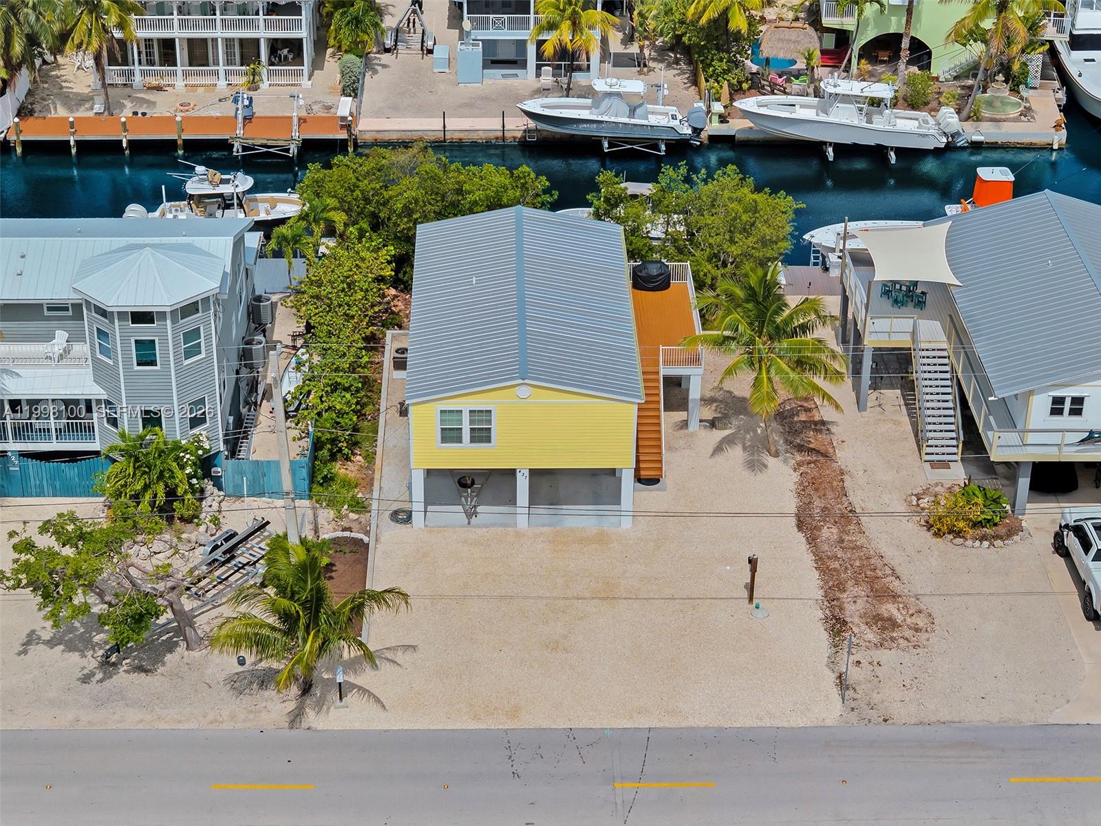 An elevated yellow house with a metal roof sits on a gravel lot near water — 437 Pirates Rd, Torch Key FL 33042, TORCH KEY, FL