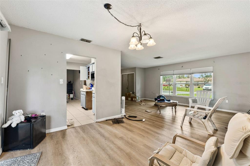 A living room with light wood-look flooring, a chandelier, and a view into the kitchen — 623 WOOD DRIVE, POINCIANA, FL