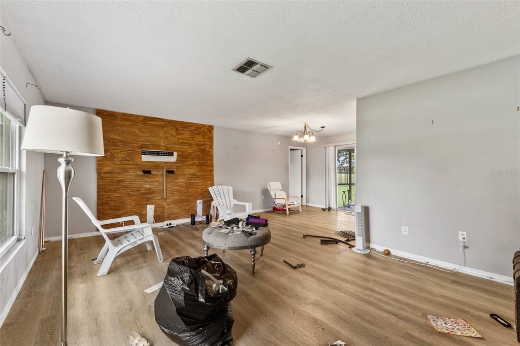 A living room with wood-look flooring, a wood-paneled accent wall, and a sliding glass door — 623 WOOD DRIVE, POINCIANA, FL