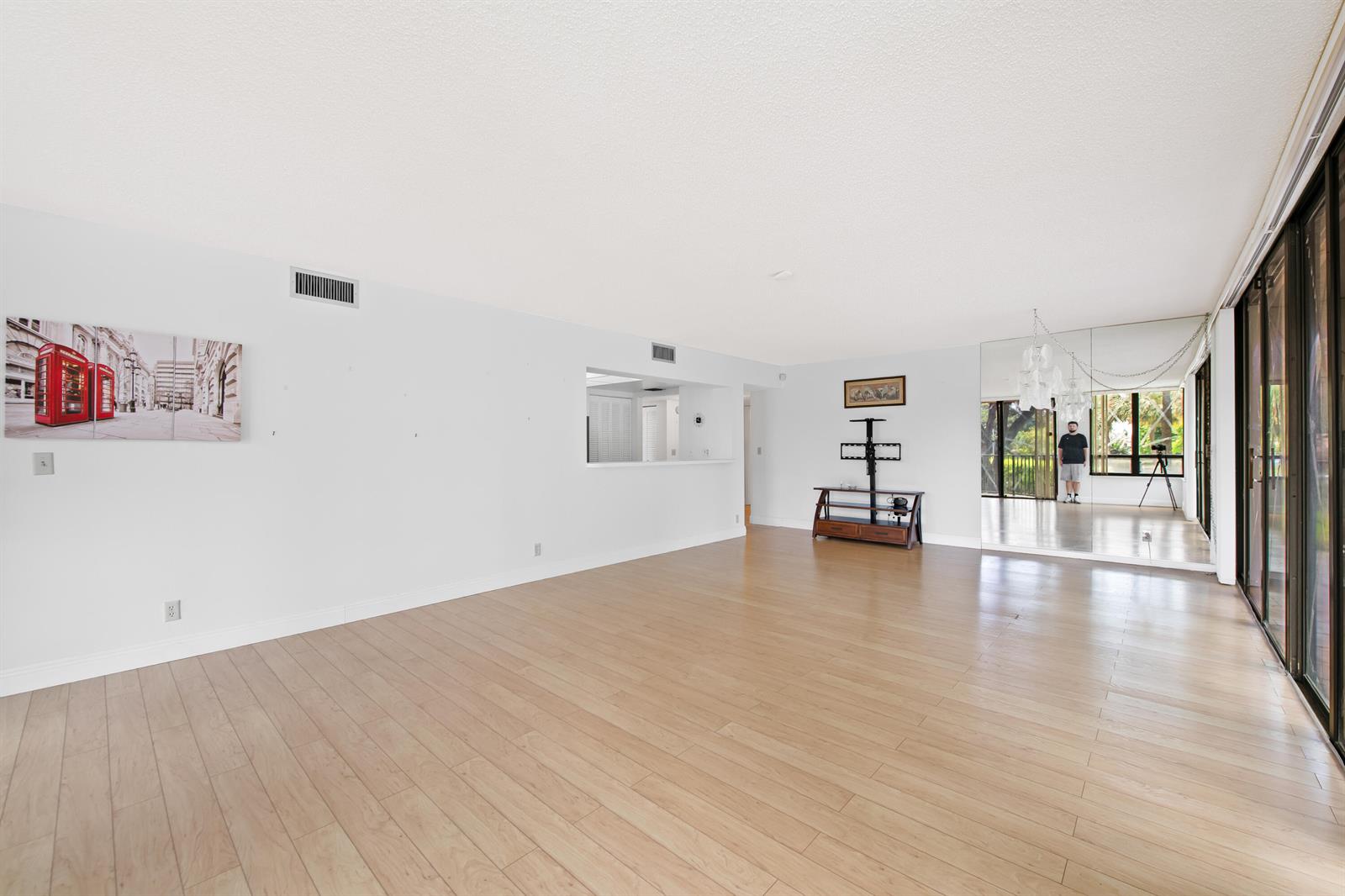 An empty living room features light wood flooring, white walls, a mirrored wall, and sliding doors — 799 Jeffery Street # 201, Boca Raton FL 33487, BOCA RATON, FL