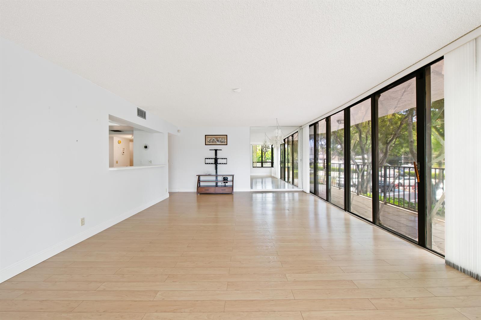 An empty living room features light wood flooring, white walls, and a large glass balcony door — 799 Jeffery Street # 201, Boca Raton FL 33487, BOCA RATON, FL
