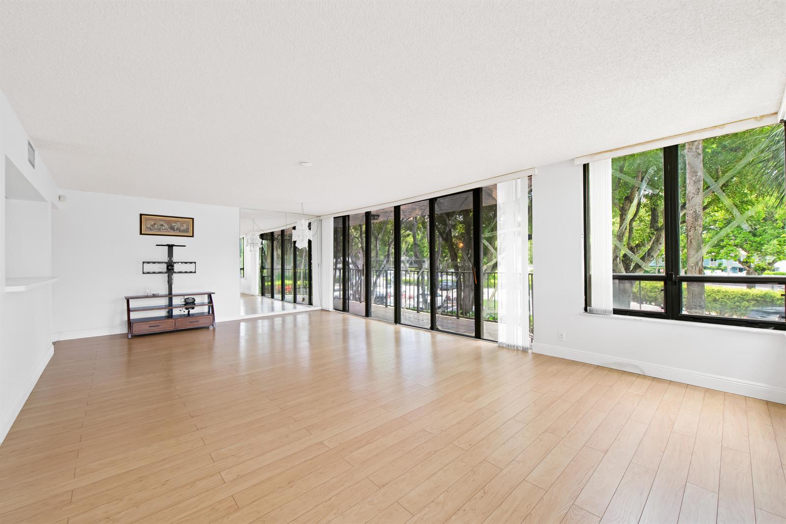 An empty living room features light wood-look flooring, white walls, and large floor-to-ceiling windows — 799 Jeffery Street # 201, Boca Raton FL 33487, BOCA RATON, FL