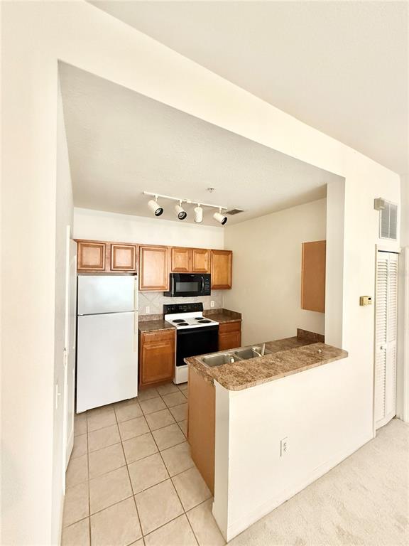 A kitchen features light wood cabinets, a white refrigerator, a black stove, and tile flooring — 6137 METROWEST BOULEVARD UNIT 306, ORLANDO, FL