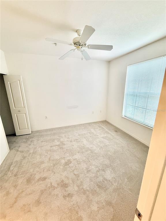 A bedroom features light gray carpeting, white walls, a ceiling fan, and a window with blinds — 6137 METROWEST BOULEVARD UNIT 306, ORLANDO, FL