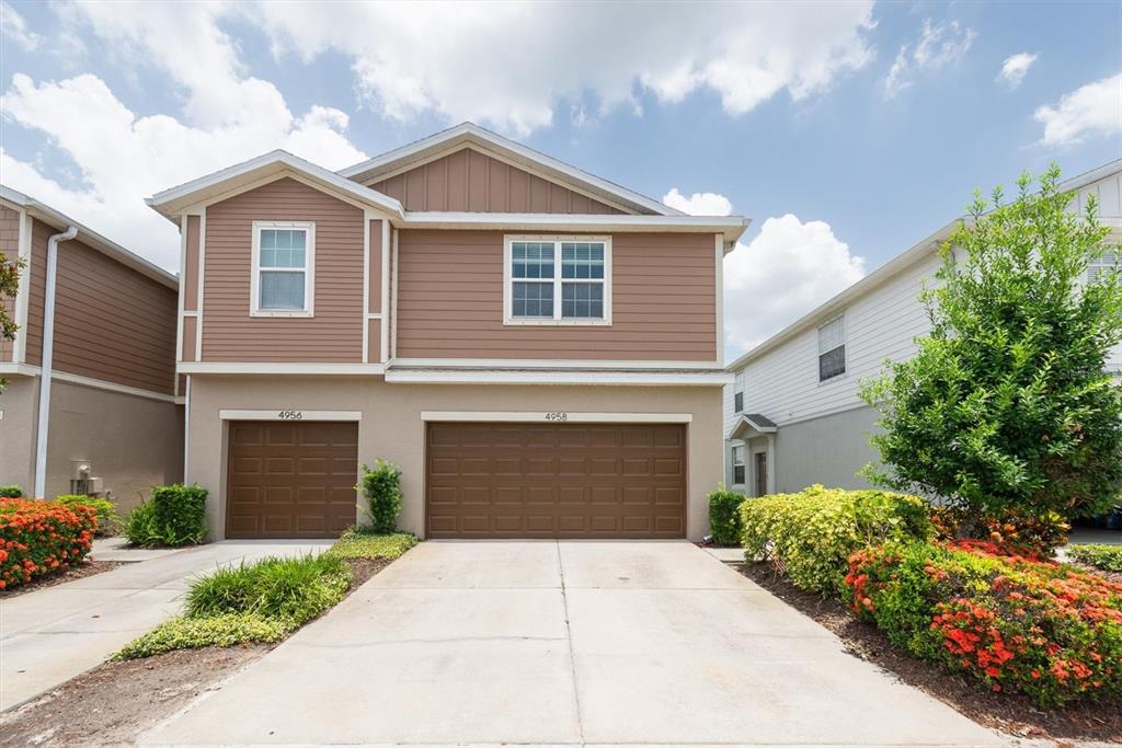 A two-story duplex with brown siding, two garage doors, and landscaped front yards — 4958 WHITE SANDERLING COURT, TAMPA, FL