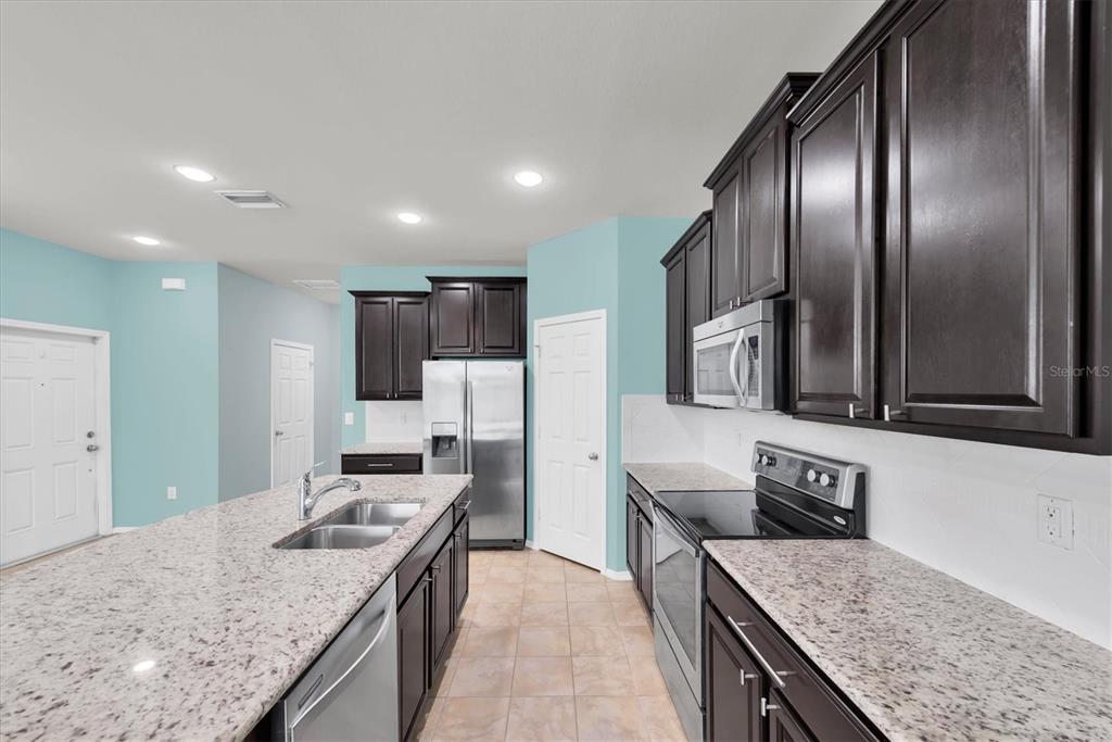 A kitchen features dark wood cabinets, granite countertops, stainless steel appliances, and light blue walls — 4958 WHITE SANDERLING COURT, TAMPA, FL