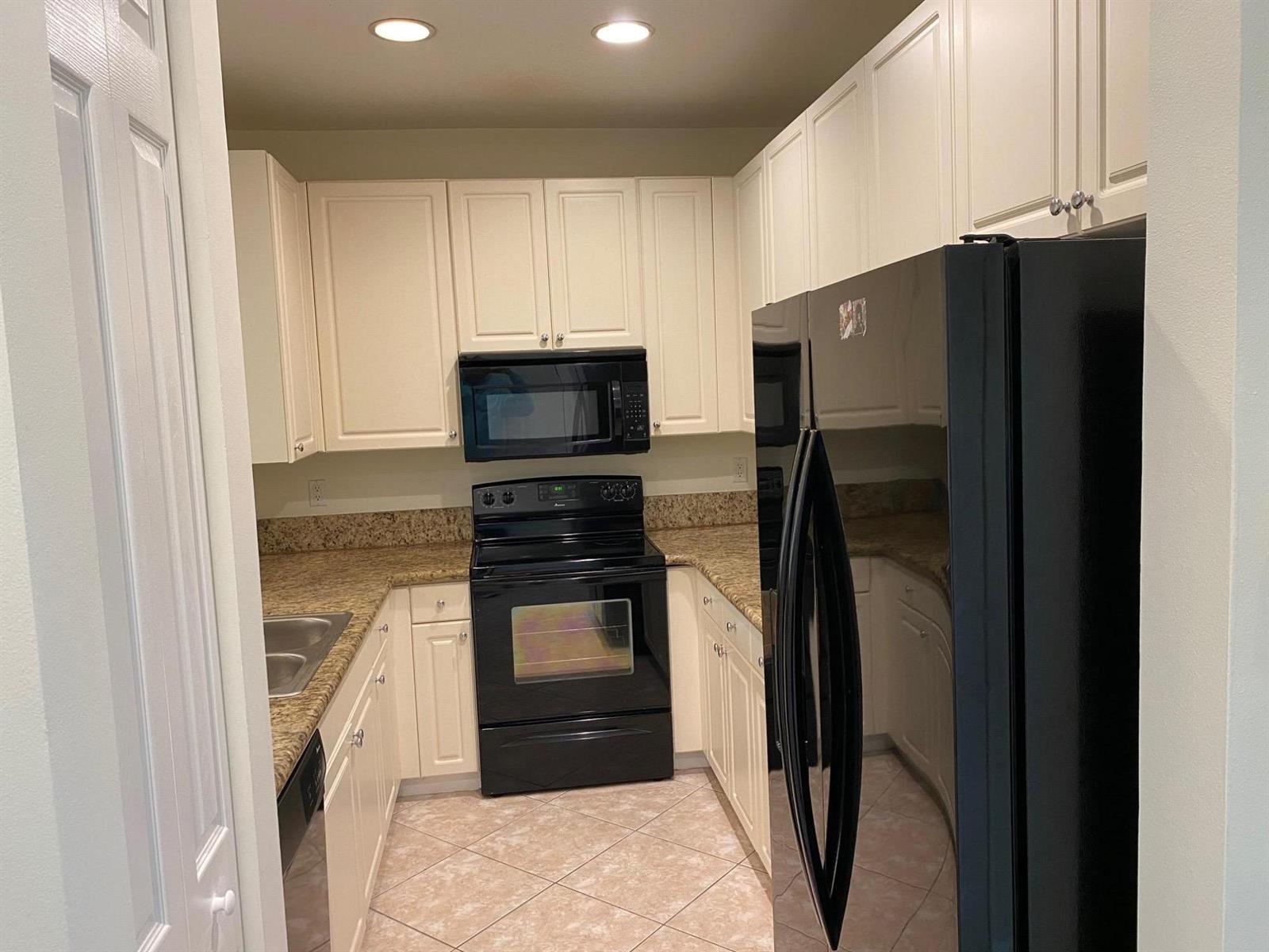A kitchen features white cabinets, black appliances, and tan granite countertops with tile flooring — 1272 Via Fiume, Boynton Beach FL 33426, BOYNTON BEACH, FL