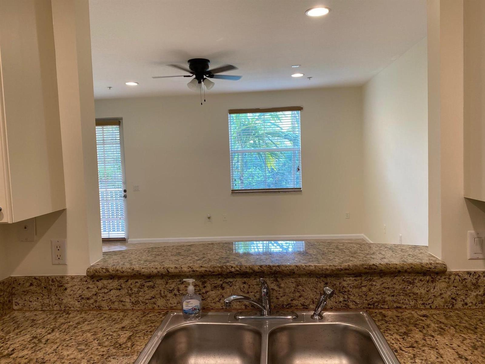 A kitchen sink with granite countertops overlooks an adjacent living area with a ceiling fan — 1272 Via Fiume, Boynton Beach FL 33426, BOYNTON BEACH, FL