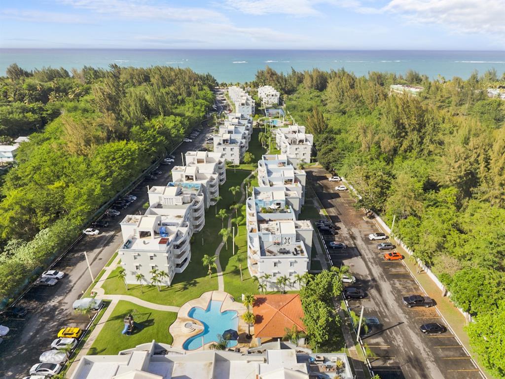 An aerial view shows a multi-building apartment complex with a central pool and parking lots — 1 OCEAN POINT UNIT 2603, LOIZA, PR