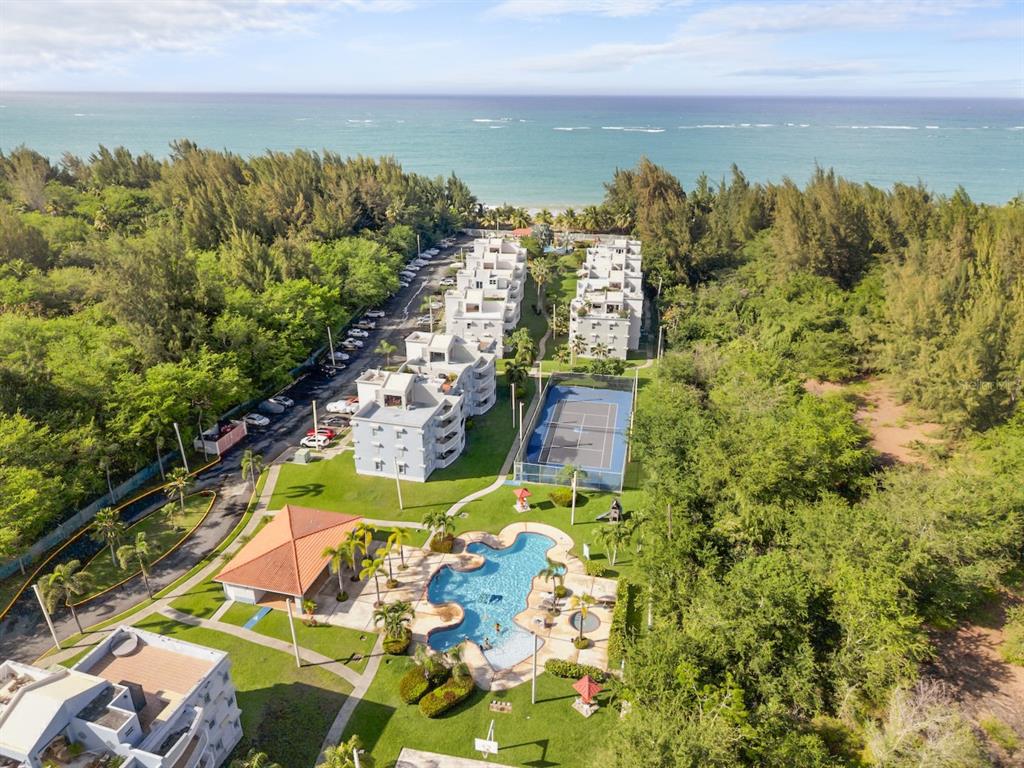 An aerial view shows a coastal apartment complex with a swimming pool and tennis court — 1 OCEAN POINT UNIT 2603, LOIZA, PR