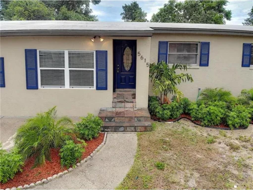 A tan house exterior features a dark blue front door, blue shutters, and landscaped front yard — 5615 ARUNDEL DRIVE, ORLANDO, FL