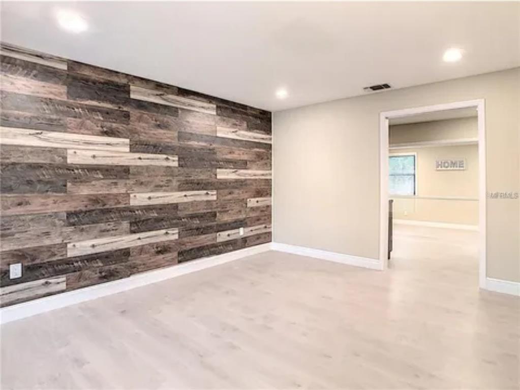 A room with light wood flooring and an accent wall featuring horizontal reclaimed wood planks — 5615 ARUNDEL DRIVE, ORLANDO, FL