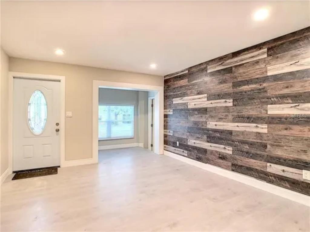An interior room features light-colored flooring, a white front door, and a rustic wood-plank accent wall — 5615 ARUNDEL DRIVE, ORLANDO, FL