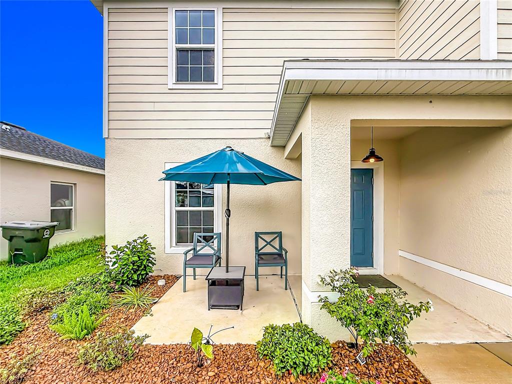 A small patio with two chairs and a blue umbrella sits outside a house entrance — 1586 TEXAS AVENUE, SUMTERVILLE, FL