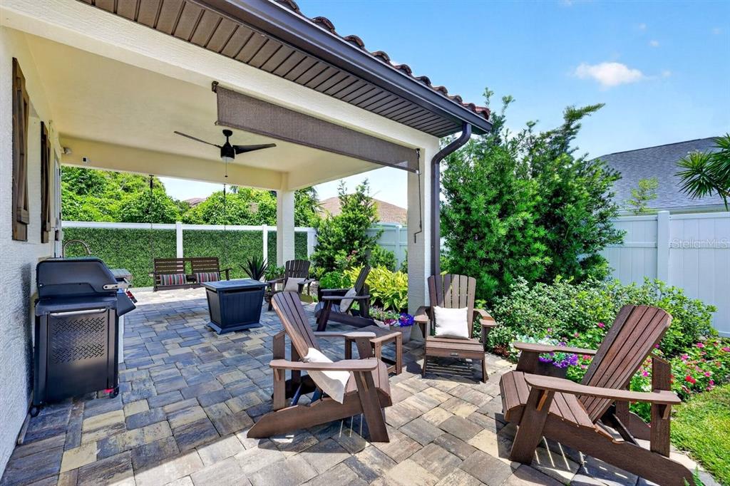A paved patio features a covered seating area with Adirondack chairs, a grill, and landscaping — 114 COQUINA KEY DRIVE, ORMOND BEACH, FL