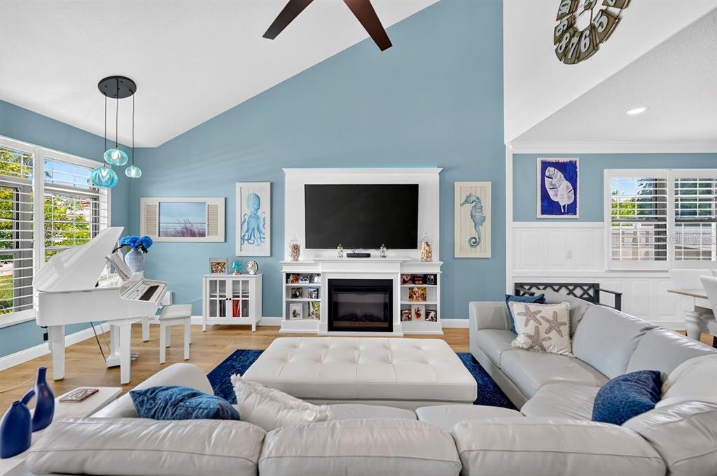 A living room features a white piano, a fireplace with a television, and blue walls — 114 COQUINA KEY DRIVE, ORMOND BEACH, FL