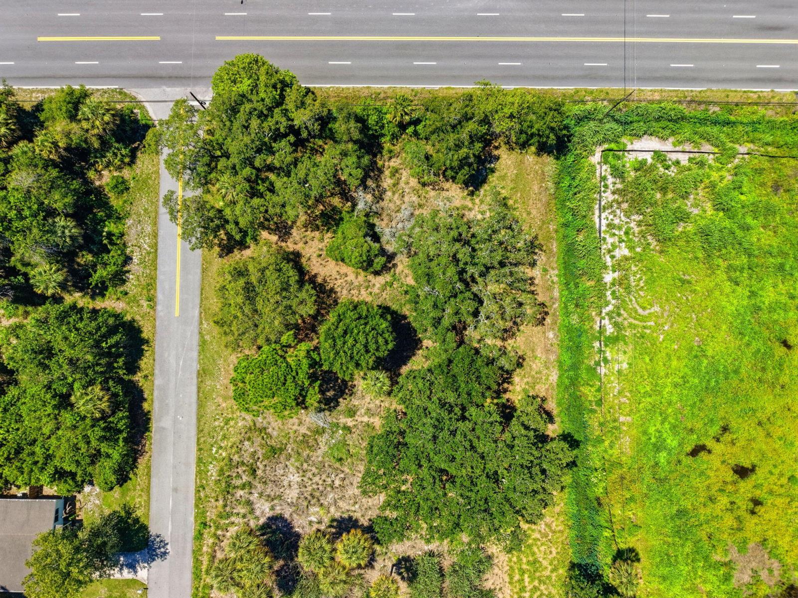 An aerial view shows a wooded lot situated between a paved road and a grassy field — 0 Aurora Road, Melbourne FL 32935, MELBOURNE, FL
