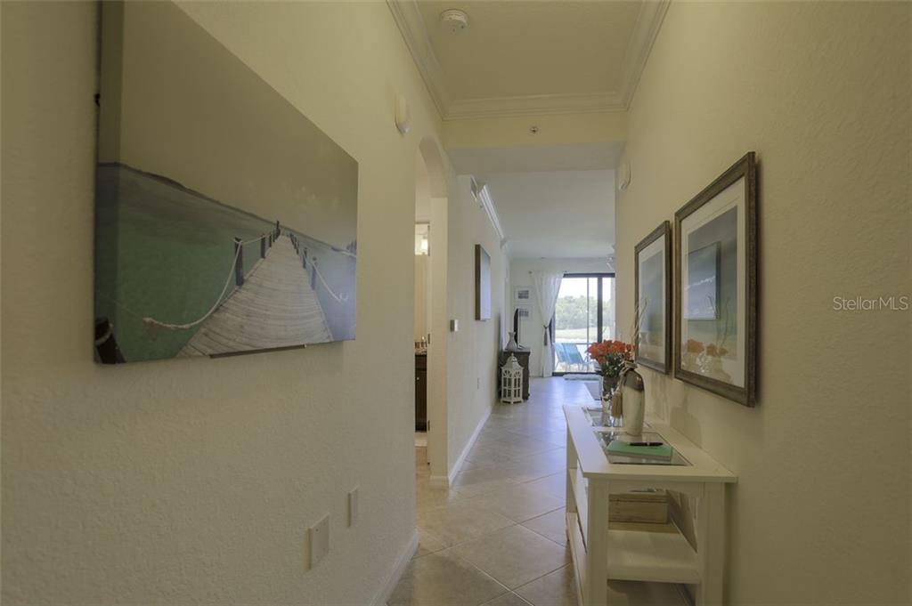 A hallway with tile flooring leads toward a living area with a view of water — 16814 VARDON TERRACE UNIT 105, LAKEWOOD RANCH, FL