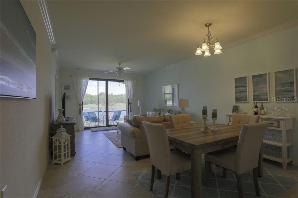 A dining area and living room with tile floors, a chandelier, and a sliding glass door — 16814 VARDON TERRACE UNIT 105, LAKEWOOD RANCH, FL
