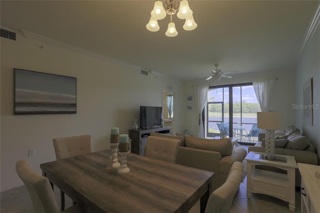 A dining area with a wood table opens into a living room with sliding glass doors — 16814 VARDON TERRACE UNIT 105, LAKEWOOD RANCH, FL