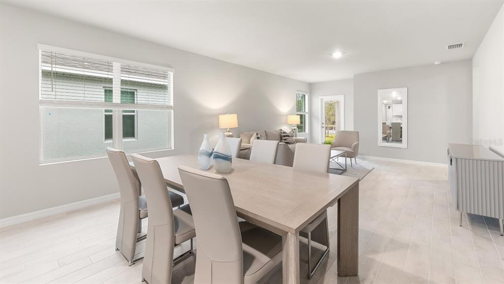A dining area with a light wood table and chairs opens into a living room — 26206 SACRED LOTUS LANE, PUNTA GORDA, FL