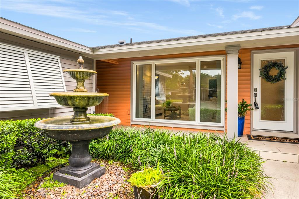A three-tiered stone fountain stands in front of a house with orange siding and shutters — 2504 FORFARSHIRE DRIVE, WINTER PARK, FL