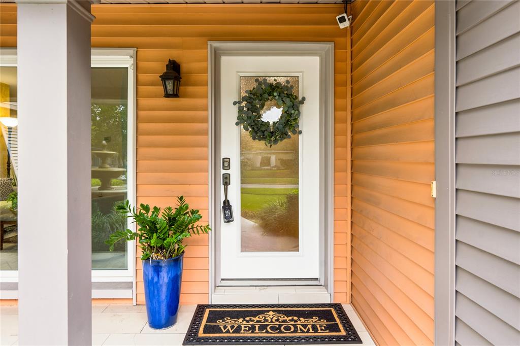 A white front door with a wreath and welcome mat sits on an orange-sided porch — 2504 FORFARSHIRE DRIVE, WINTER PARK, FL