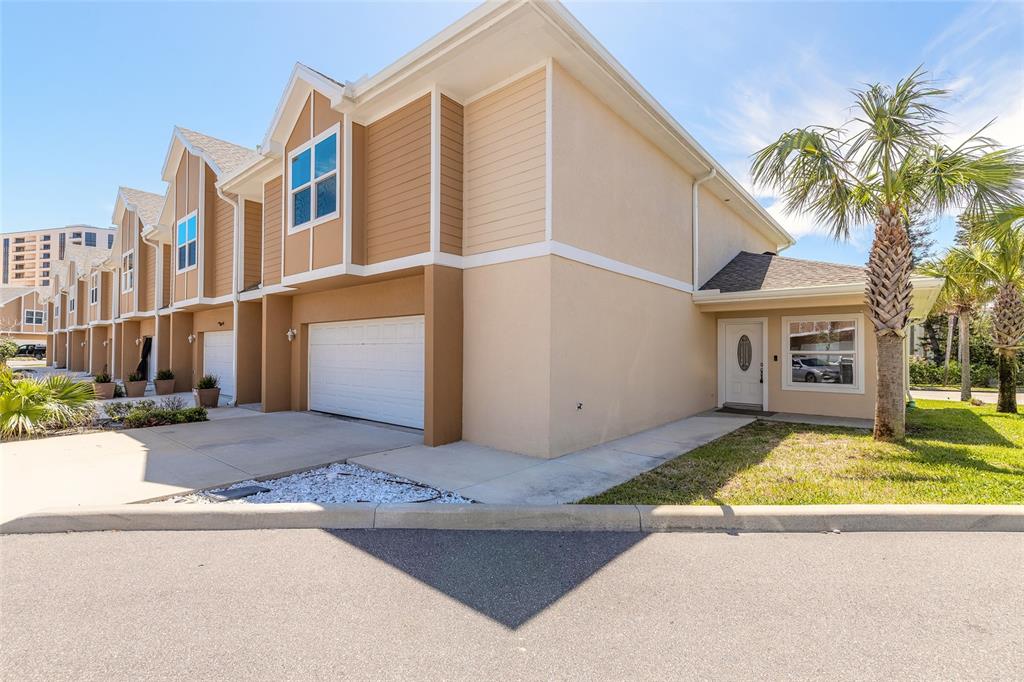 A row of tan townhouses with white garage doors and a palm tree in front — 119 OCEANS CIRCLE, DAYTONA BEACH SHORES, FL