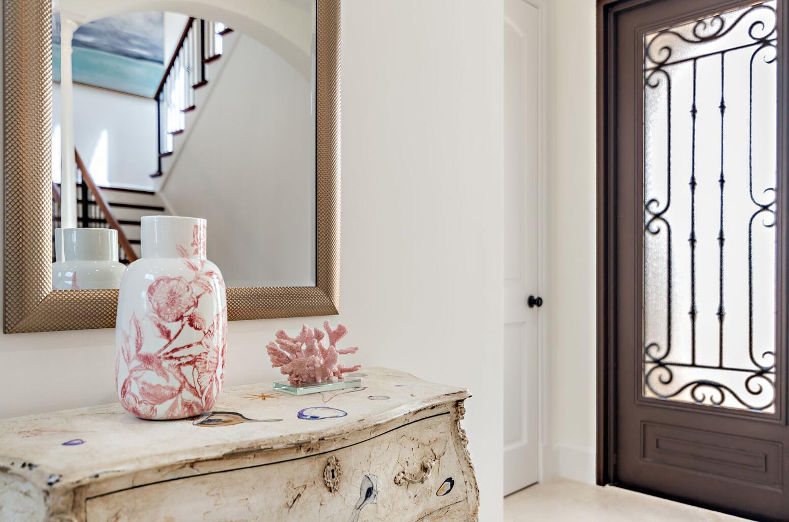 A foyer features a distressed white chest, a floral vase, and a mirror reflecting stairs — 141 Gregory Place, West Palm Beach FL 33405, WEST PALM BEACH, FL