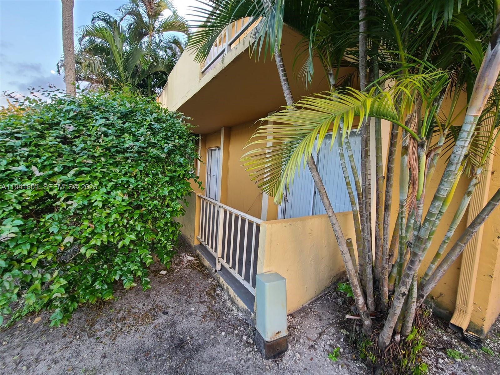A ground-level patio with a metal railing sits beside a yellow building and palm trees — 18111 NW 68th Ave # G106, Hialeah FL 33015, HIALEAH, FL