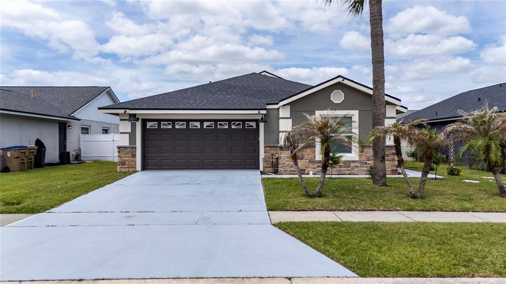 A single-story house with a dark garage door, stone accents, and a paved driveway — 3254 MOCCASIN DRIVE, KISSIMMEE, FL