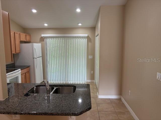 A kitchen with granite countertops, light wood cabinets, a white refrigerator, and vertical blinds — 113 BRUNSWICK LANE UNIT B, PALM COAST, FL