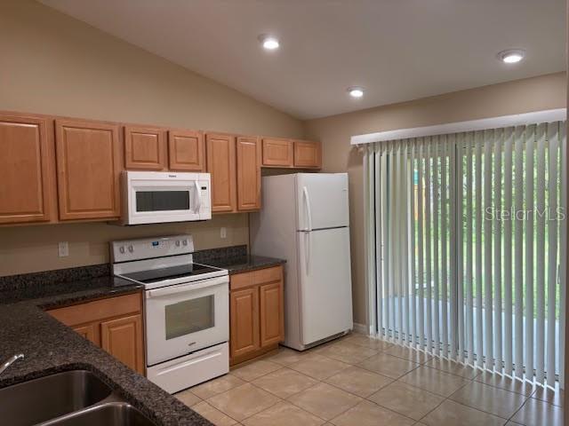A kitchen with wood cabinets, white appliances, dark countertops, and a sliding glass door — 113 BRUNSWICK LANE UNIT B, PALM COAST, FL