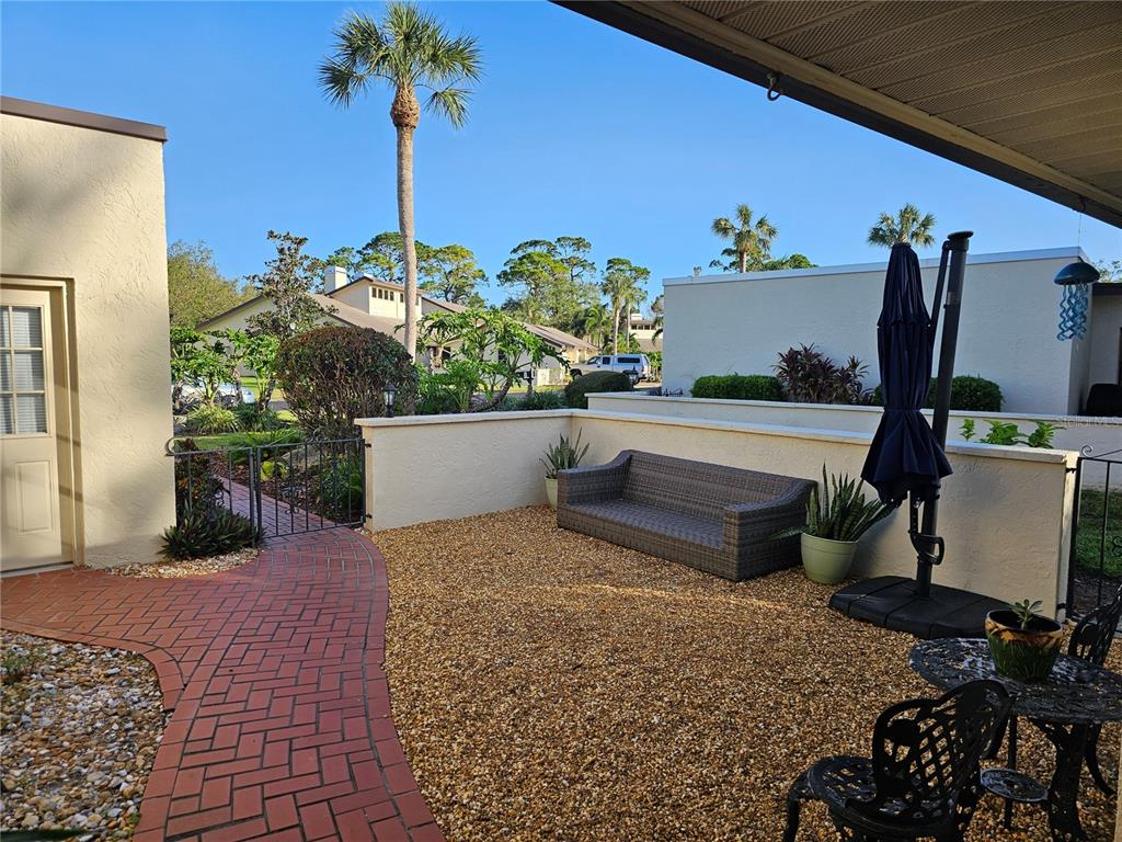 A patio features a brick walkway, gravel ground, a wicker sofa, and a patio umbrella — 4522 LA JOLLA DRIVE, BRADENTON, FL