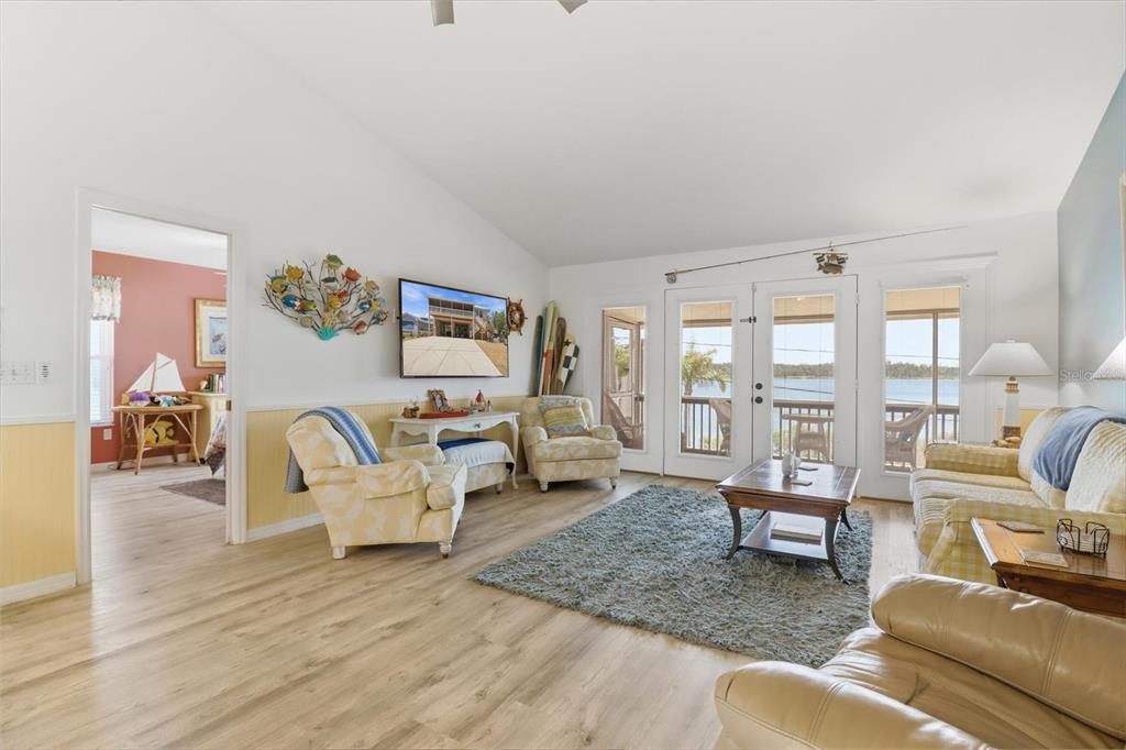 A living room features light wood flooring, yellow wainscoting, and glass doors overlooking a lake — 2882 N COMANCHE POINT, CRYSTAL RIVER, FL