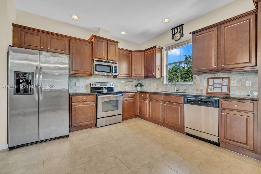 A kitchen features wood cabinets, stainless steel appliances, granite countertops, and tile flooring — 4357 Cascada Cir # 4357, Cooper City FL 33024, COOPER CITY, FL