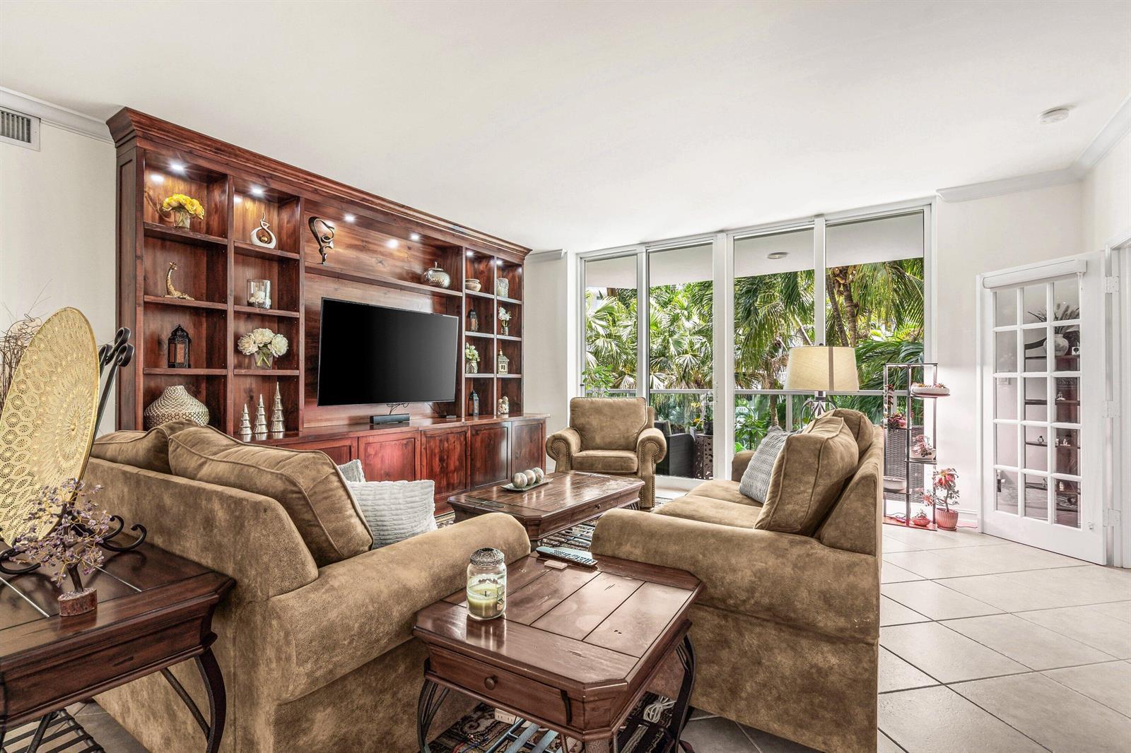 A living room features brown sofas, a large wooden media unit, and floor-to-ceiling windows — 500 SE Mizner Boulevard # A209, Boca Raton FL 33432, BOCA RATON, FL