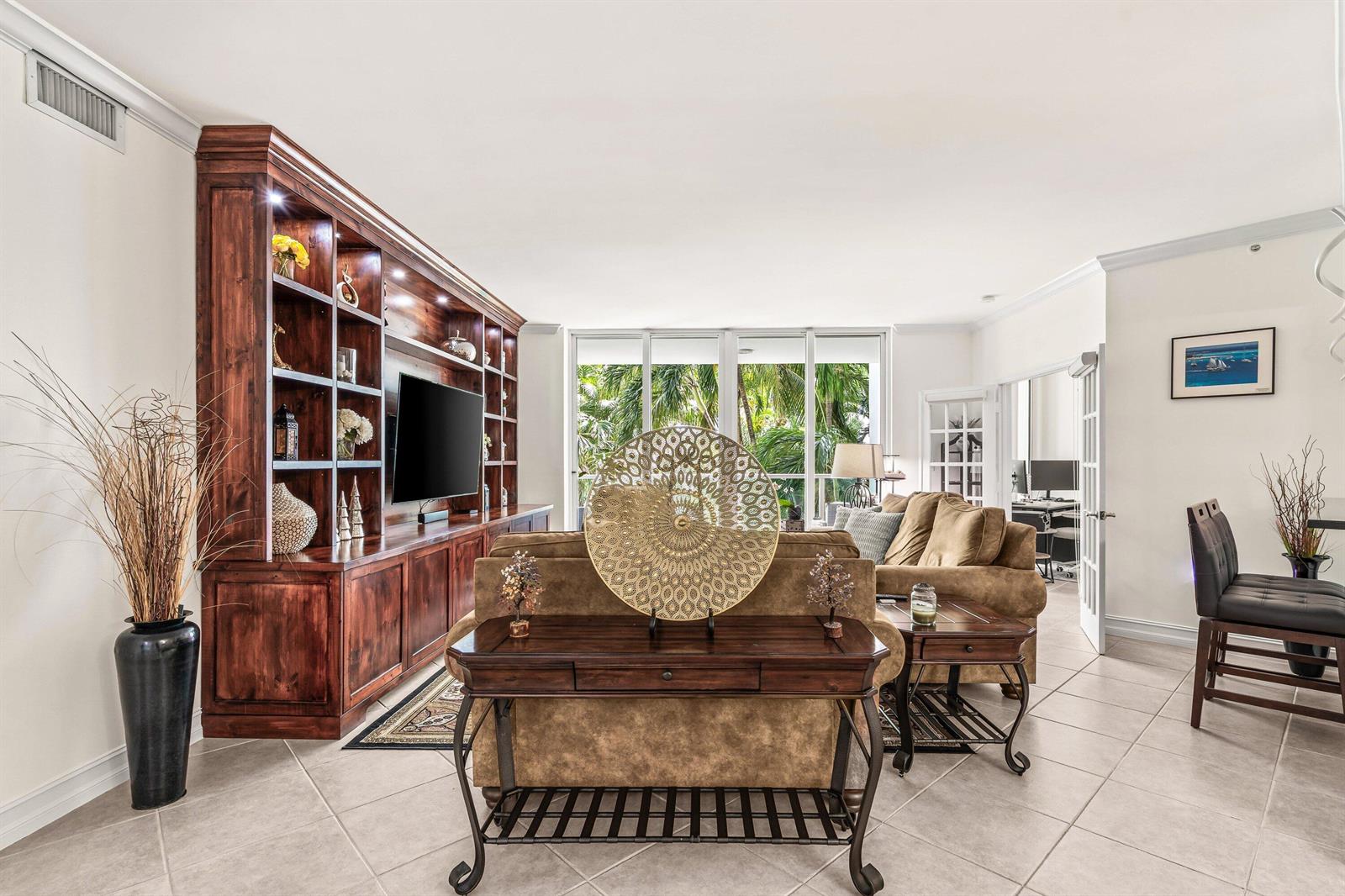 A living room features a large wooden built-in shelving unit, a sofa, and floor-to-ceiling windows — 500 SE Mizner Boulevard # A209, Boca Raton FL 33432, BOCA RATON, FL