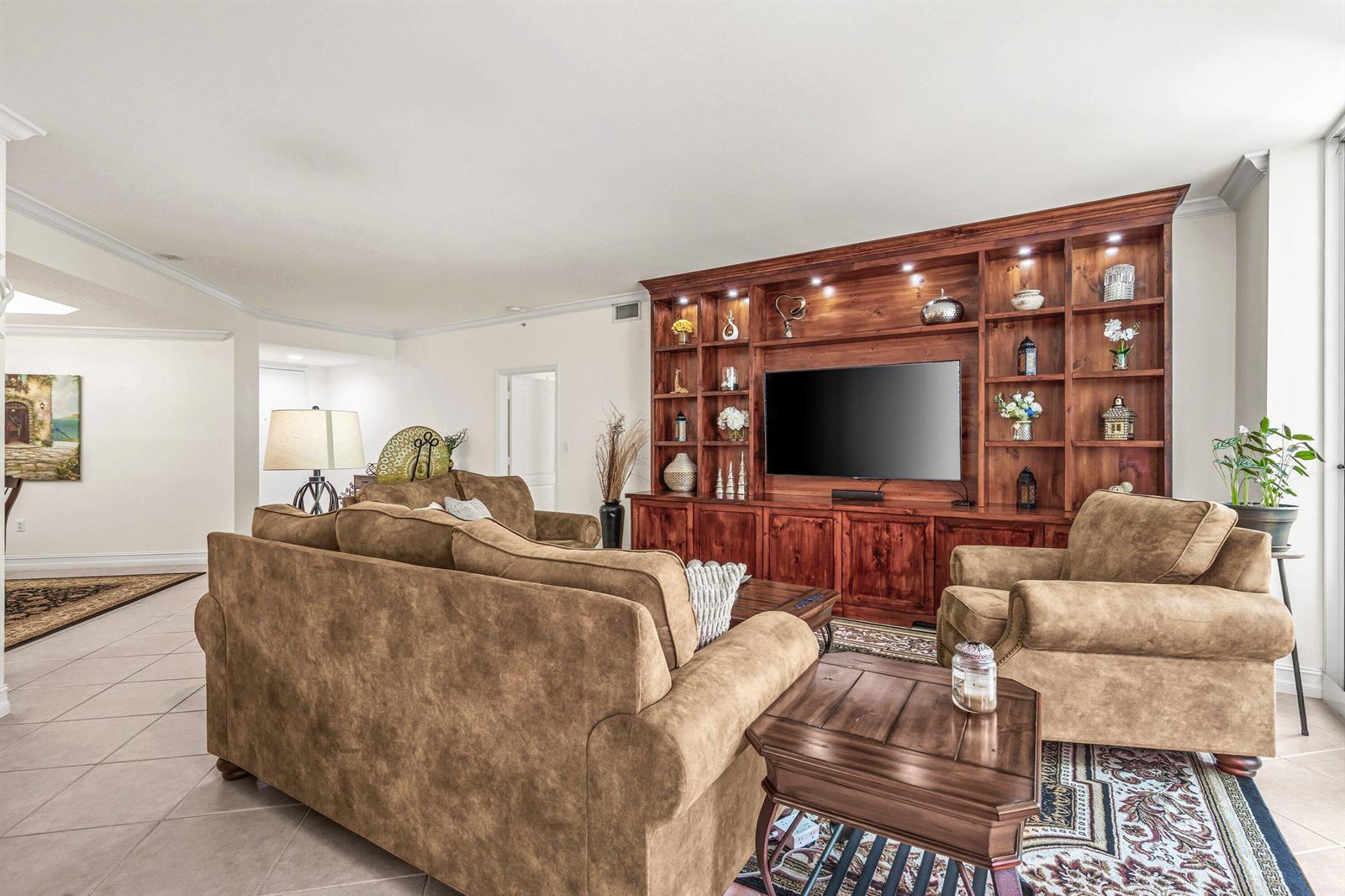 A living room features a large wooden built-in entertainment center, brown sofas, and tile flooring — 500 SE Mizner Boulevard # A209, Boca Raton FL 33432, BOCA RATON, FL
