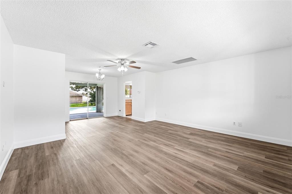 A spacious living room features light wood-look flooring, white walls, a ceiling fan, and sliding doors — 1360 N OLD MILL DRIVE, DELTONA, FL